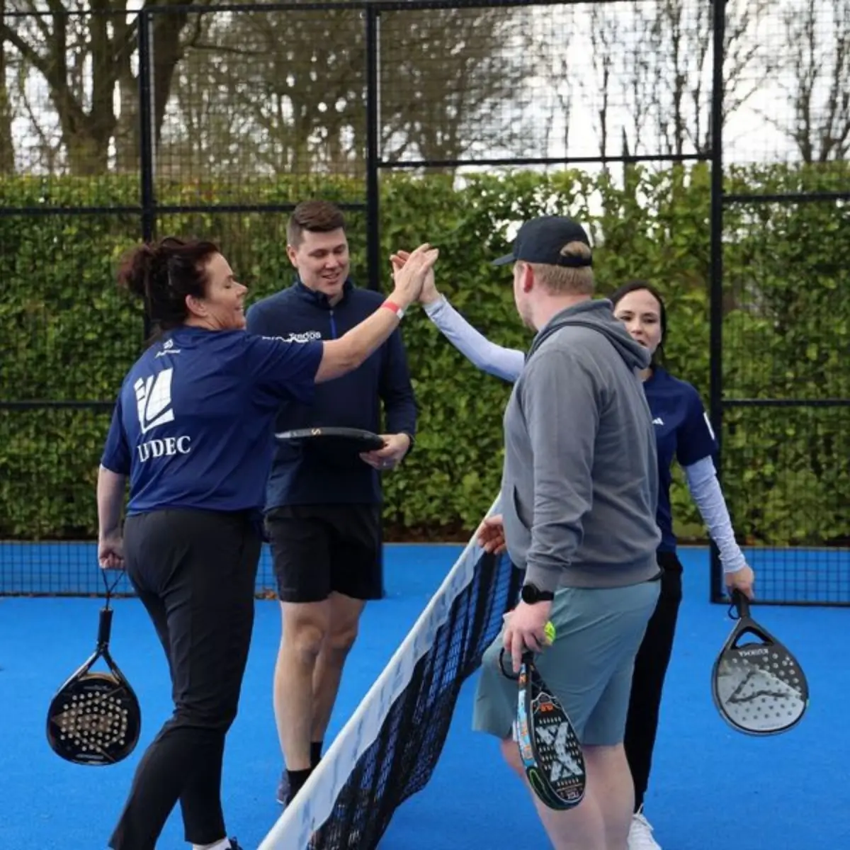 4 padelspelers die elkaar een high five geven op outdoor padelbaan