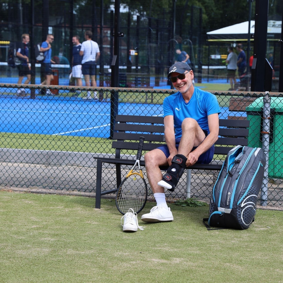 Man op een bankje bij outdoor padelbaan die zich klaarmaakt voor de wedstrijd