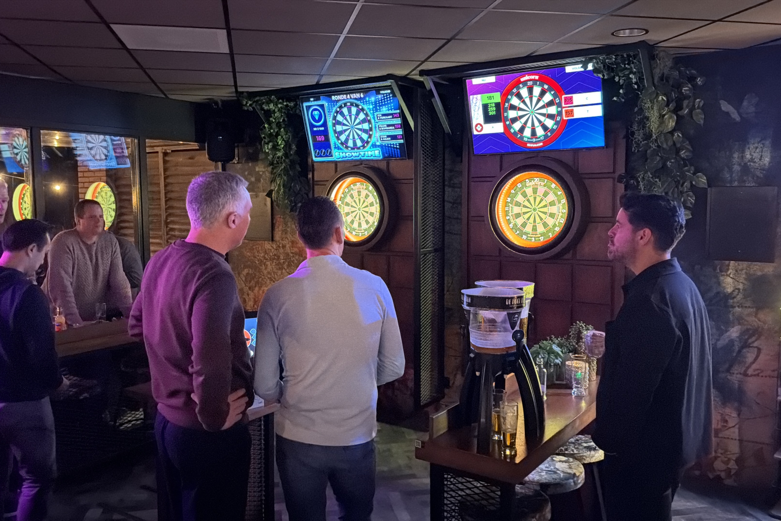 Groep mannen speelt interactief darts op twee digitale dartbanen in een sfeervolle horecaruimte van De Hoge Heide