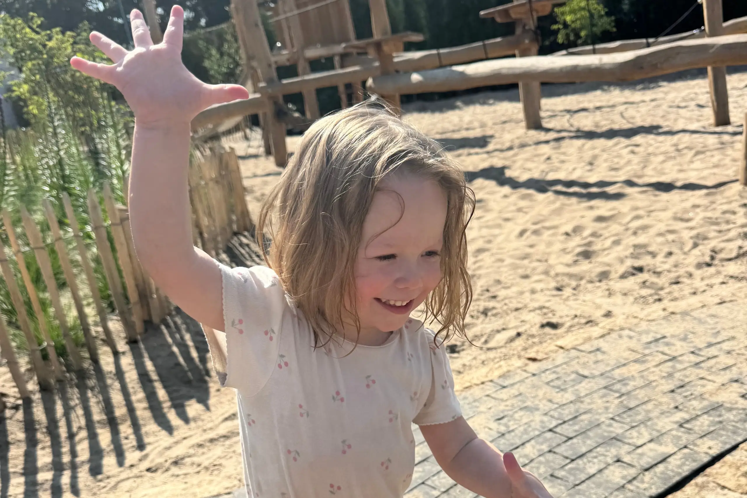 Lachend meisje steekt haar hand op tijdens het hebben van waterpret in een zonnige zandspeeltuin.